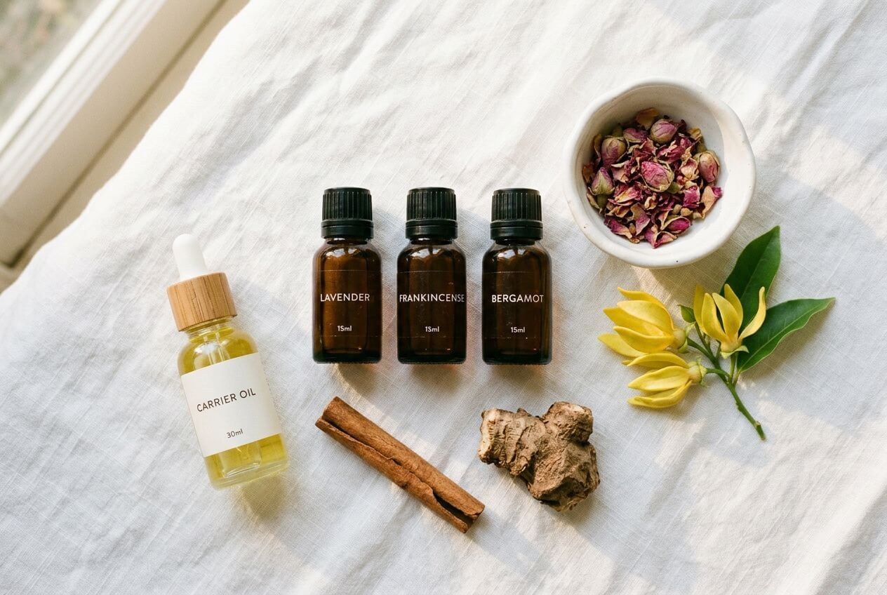 Huiles et herbes essentielles en bouteilles brunes, huile porte-goutte, cannelle, gingembre, fleurs jaunes et pétales de rose en bowl, ambiance aromathérapie naturelle pour stimuler la libido féminine.
