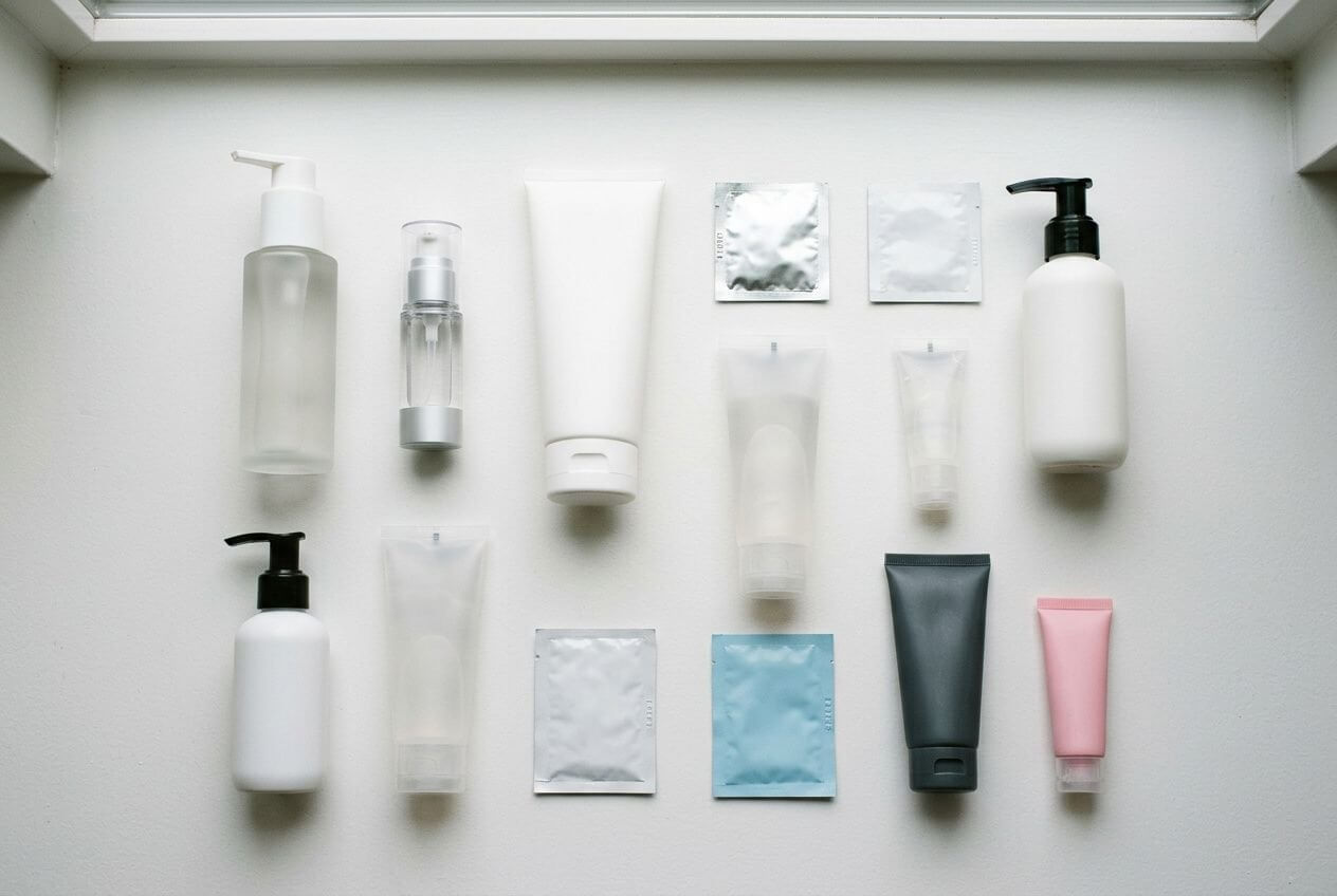 Set de produits d’hygiène intime et échantillons: flacons, tubes et sachets en rangée sur fond clair, pour guides et comparatifs.
